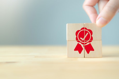 The man's hand places the wooden cubes with the red quality guarantee symbol on wooden cubes with a gray background